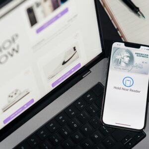 Smartphone with payment terminal app next to laptop displaying online shopping site.