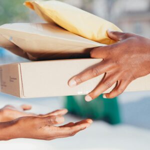 Close-up image of hands exchanging packages outdoors. Represents delivery and shipping services.