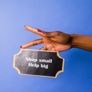 A hand holding a sign reading 'Shop small, Help big' against a blue background.